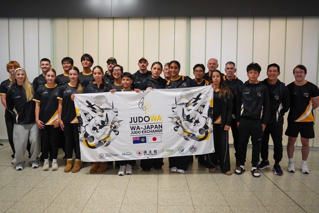 Judo WA athletes and coaches in black and gold team uniforms holding the WA–Japan Judo Exchange banner.
